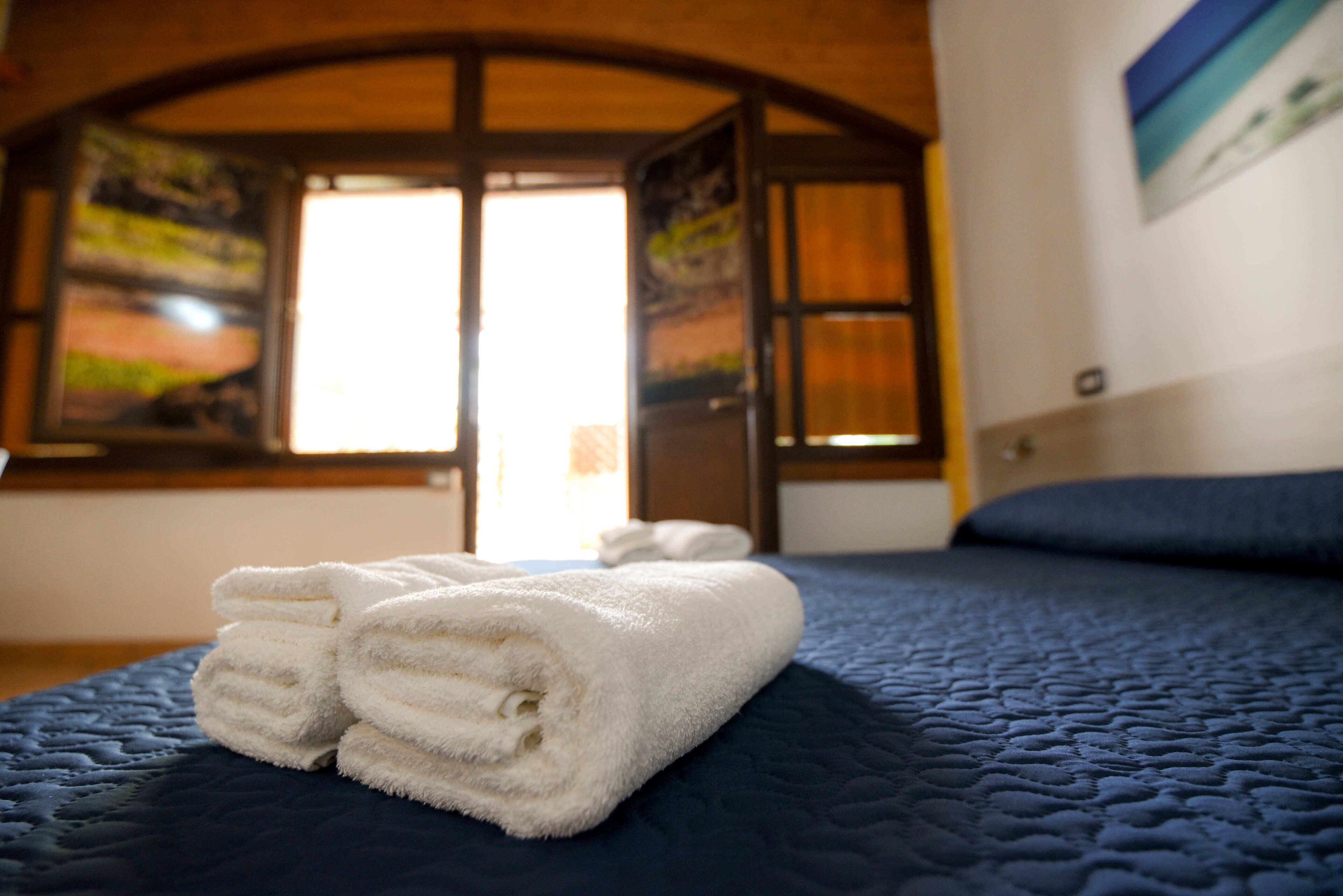 A neatly made bed with a folded white towel and a blue quilted bedspread.