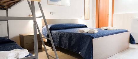 Ein Schlafzimmer mit Etagenbetten, einer Stehleiter, einem Nachttisch, einem Bett mit blauer Steppdecke und einem Bild von einer Strandansicht.