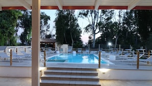 Zona de piscina con escalones que bajan al agua, rodeada de sillones de descanso y una zona de estar cubierta.