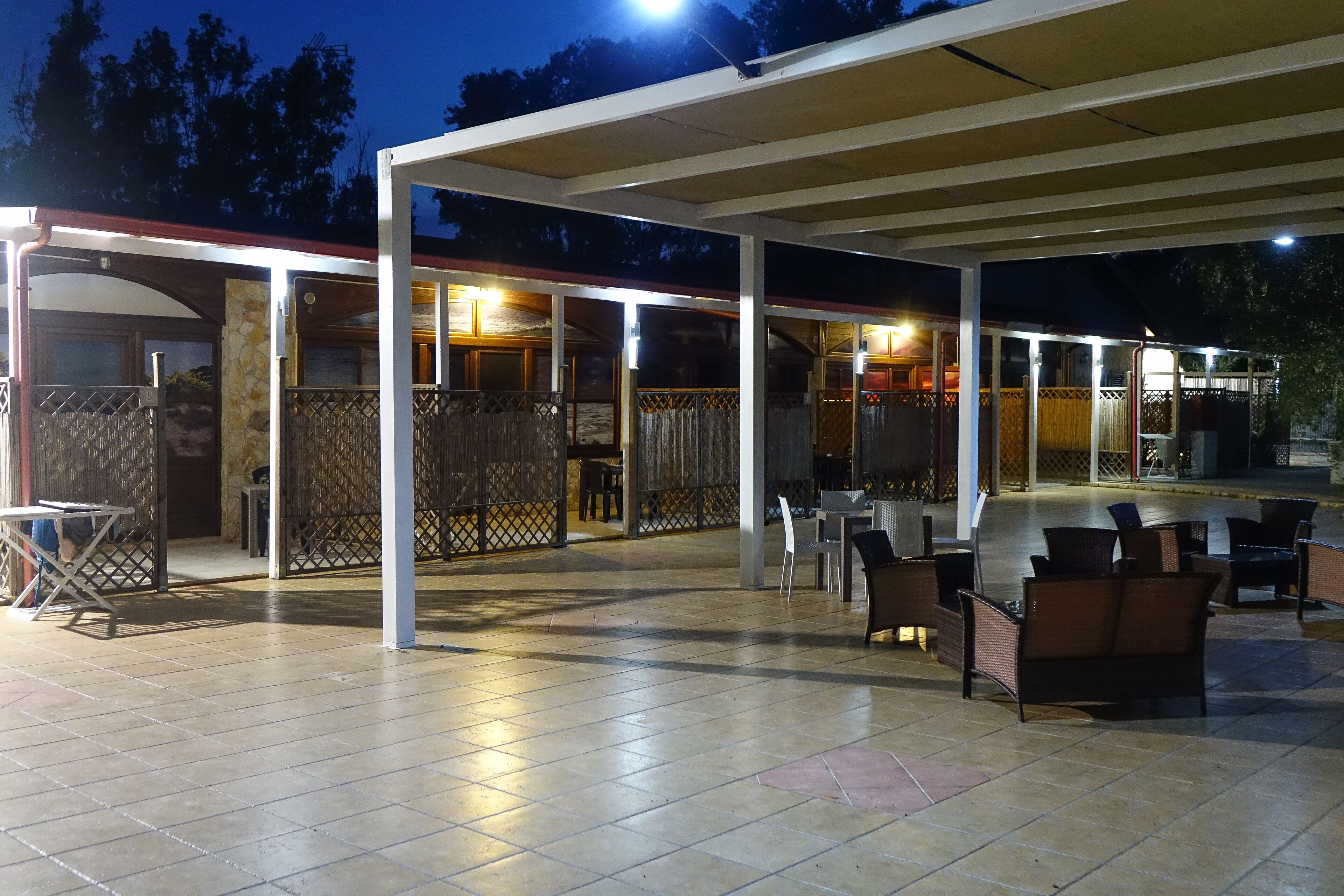 Un área de patio exterior techada con suelo de baldosas, arreglos de asientos y un espacio parcialmente cerrado con vistas a los alrededores.