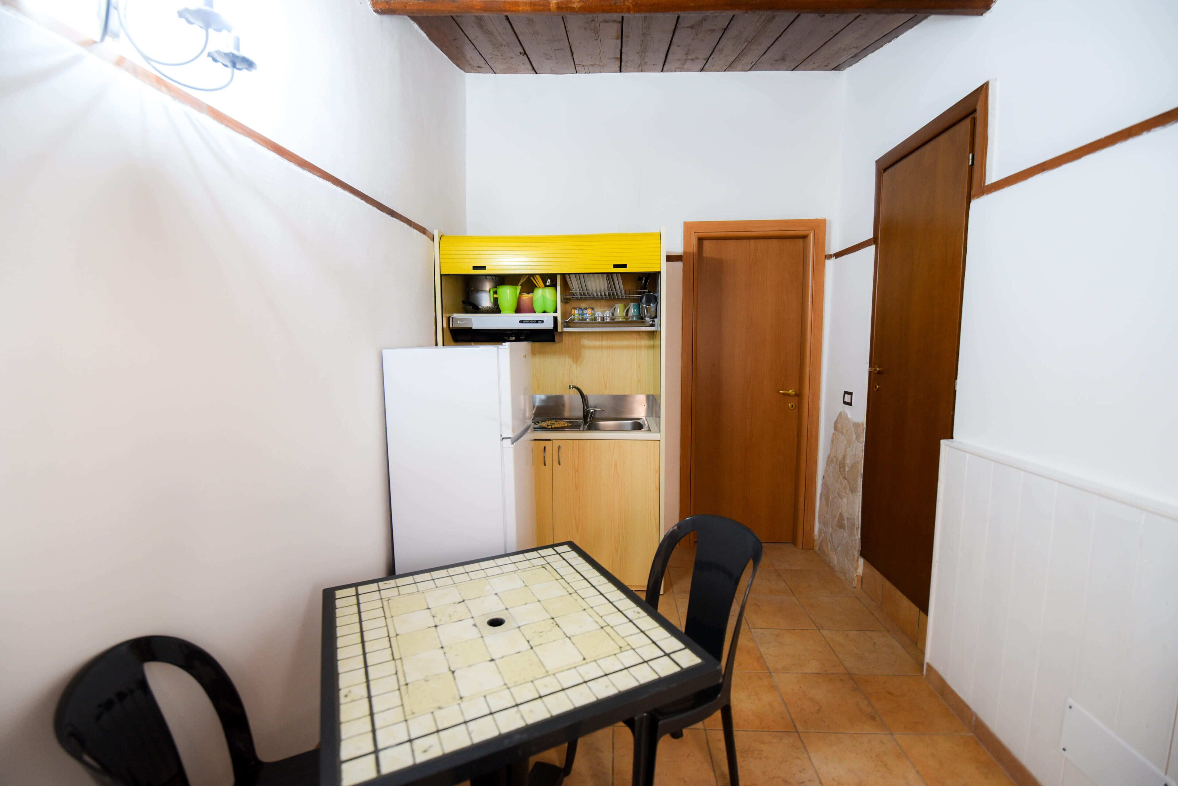 A compact kitchen with a refrigerator, a yellow cabinet, and a dining table with chairs.