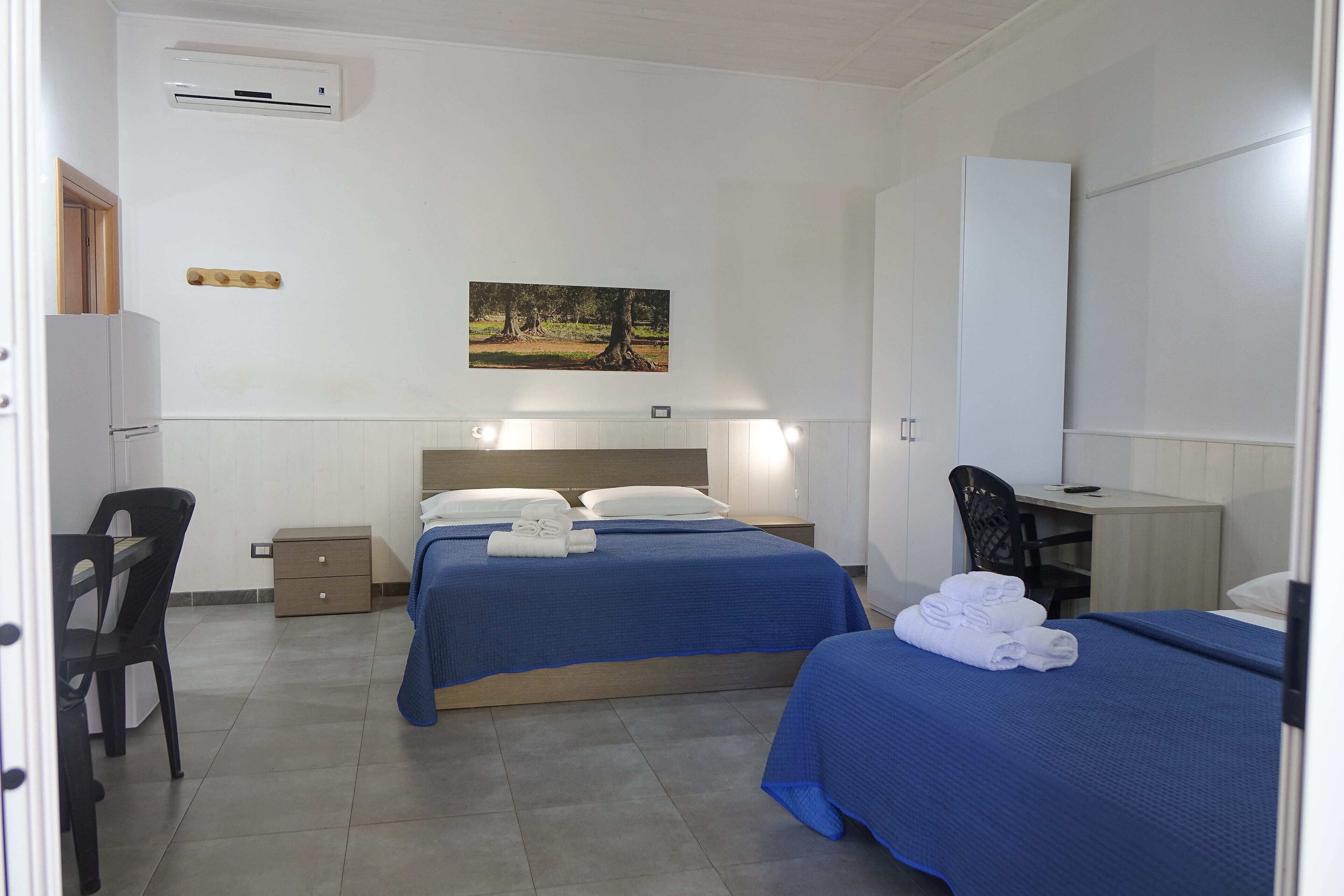 Een hotelkamer met twee bedden, een bureau, een stoel, een kledingkast en een schilderij aan de muur.