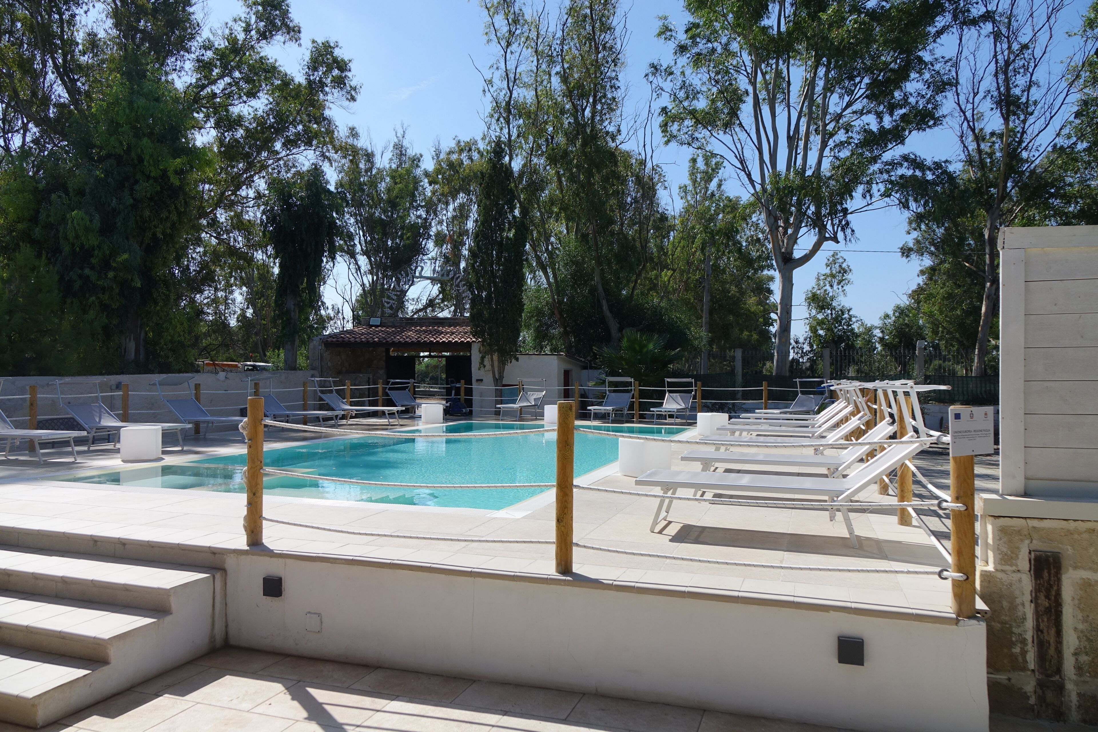 En swimmingpool med solstolar och en liten byggnad i bakgrunden.