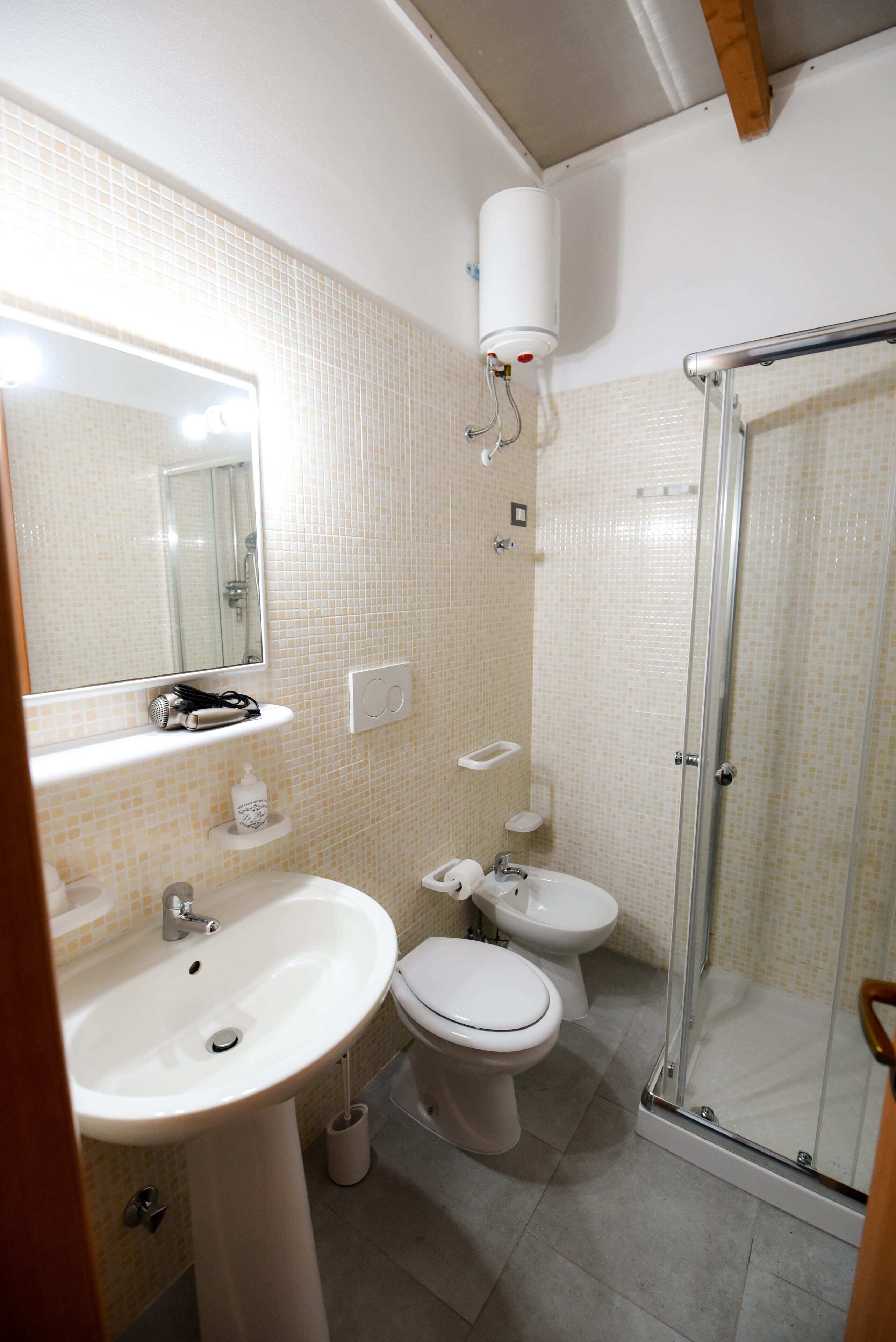Un baño con lavamanos, dos inodoros, un espejo y ducha con mampara de vidrio.