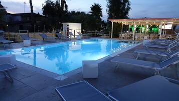 Relax by the tranquil pool surrounded by lounge chairs and palm trees.