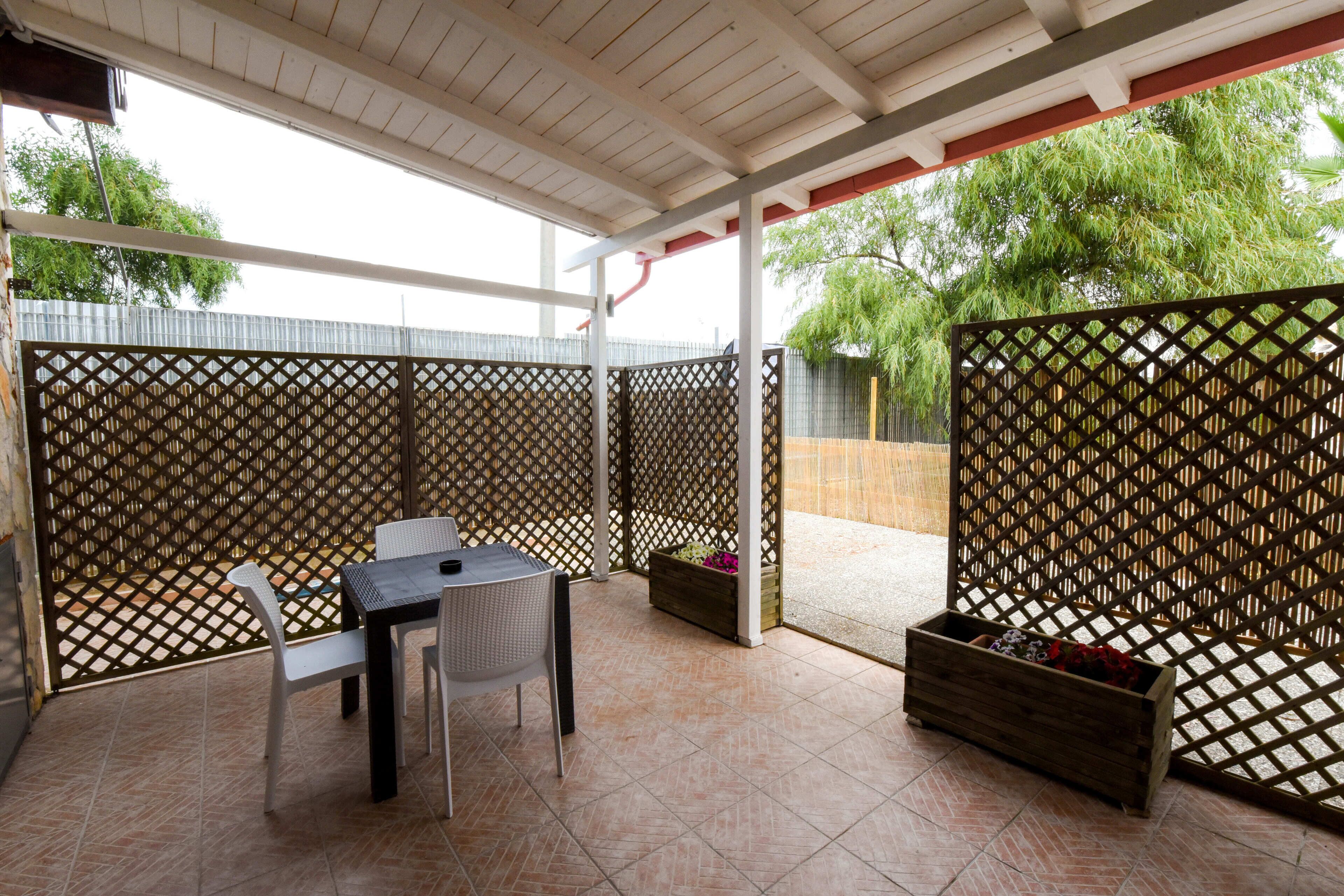 A covered patio area with a table and chairs, a wooden planter, and a lattice fence.