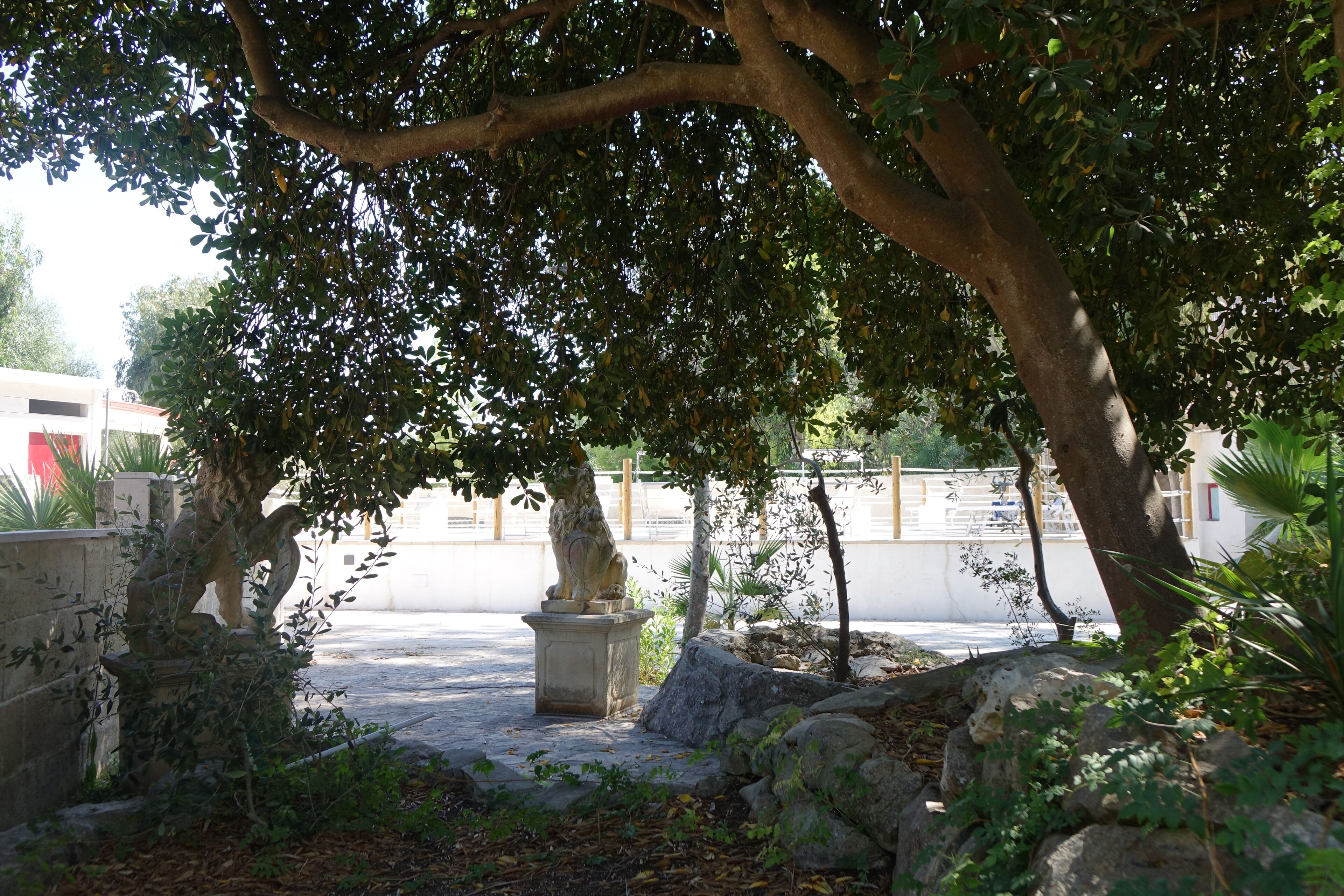 A courtyard with stone statues, a stone wall, and a paved area surrounded by trees and plants.
