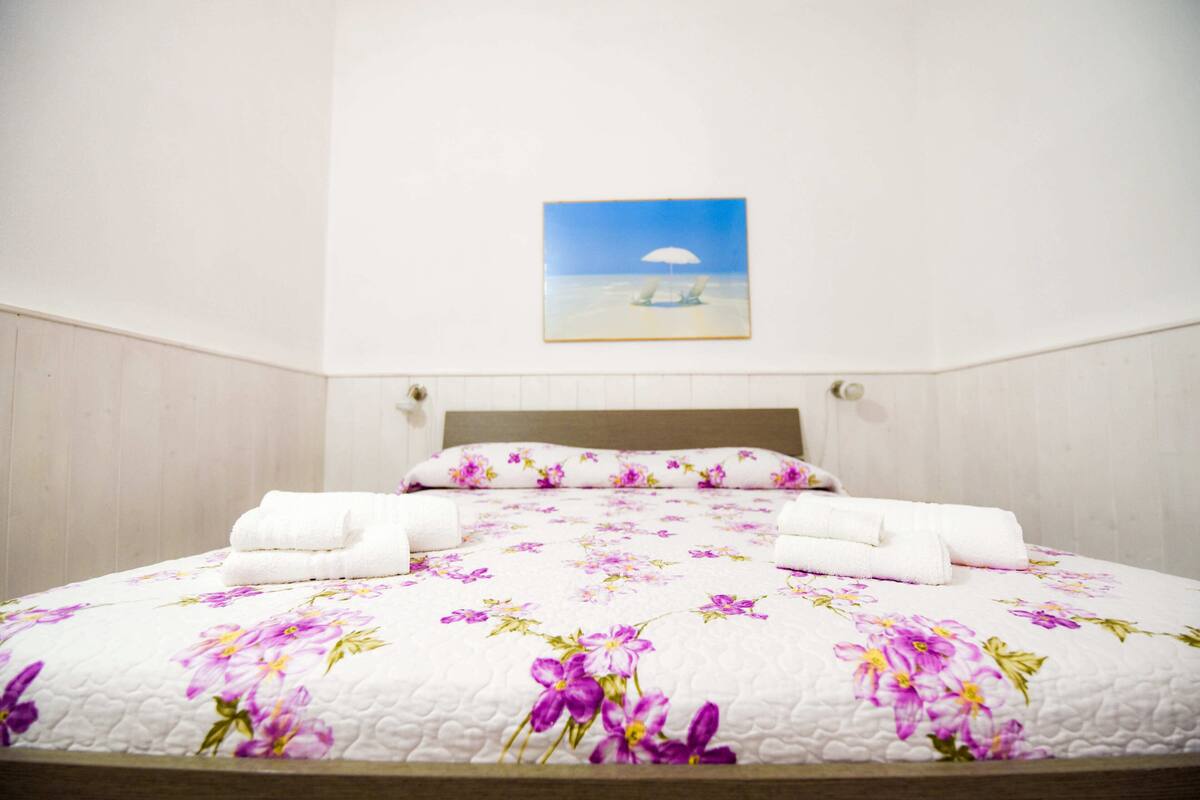 Een opgemaakt bed met een bloemenbedekker en twee keurig gevouwen witte handdoeken.
