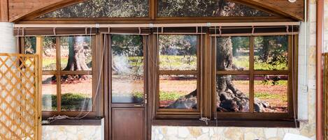 Un patio cubierto con paredes de piedra, ventanas grandes y una mesa con una silla.