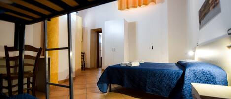 A room with a bed, a chair, and a desk. There is a door leading to another room.