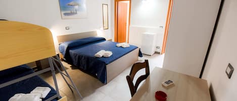 Habitación de hotel con literas, una cama individual, una mesa de madera, una silla, un cuenco pequeño rojo y una lámpara fijada a la pared.