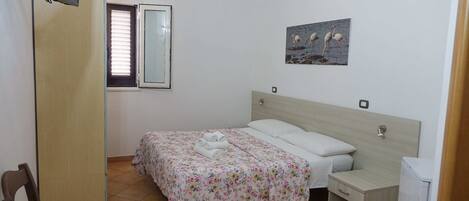 Une chambre à coucher avec un lit, une table de chevet, une chaise, une télévision, une fenêtre et un tableau au mur.