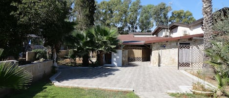 A residential property with a paved driveway, stone walls, and a fenced yard with palm trees.