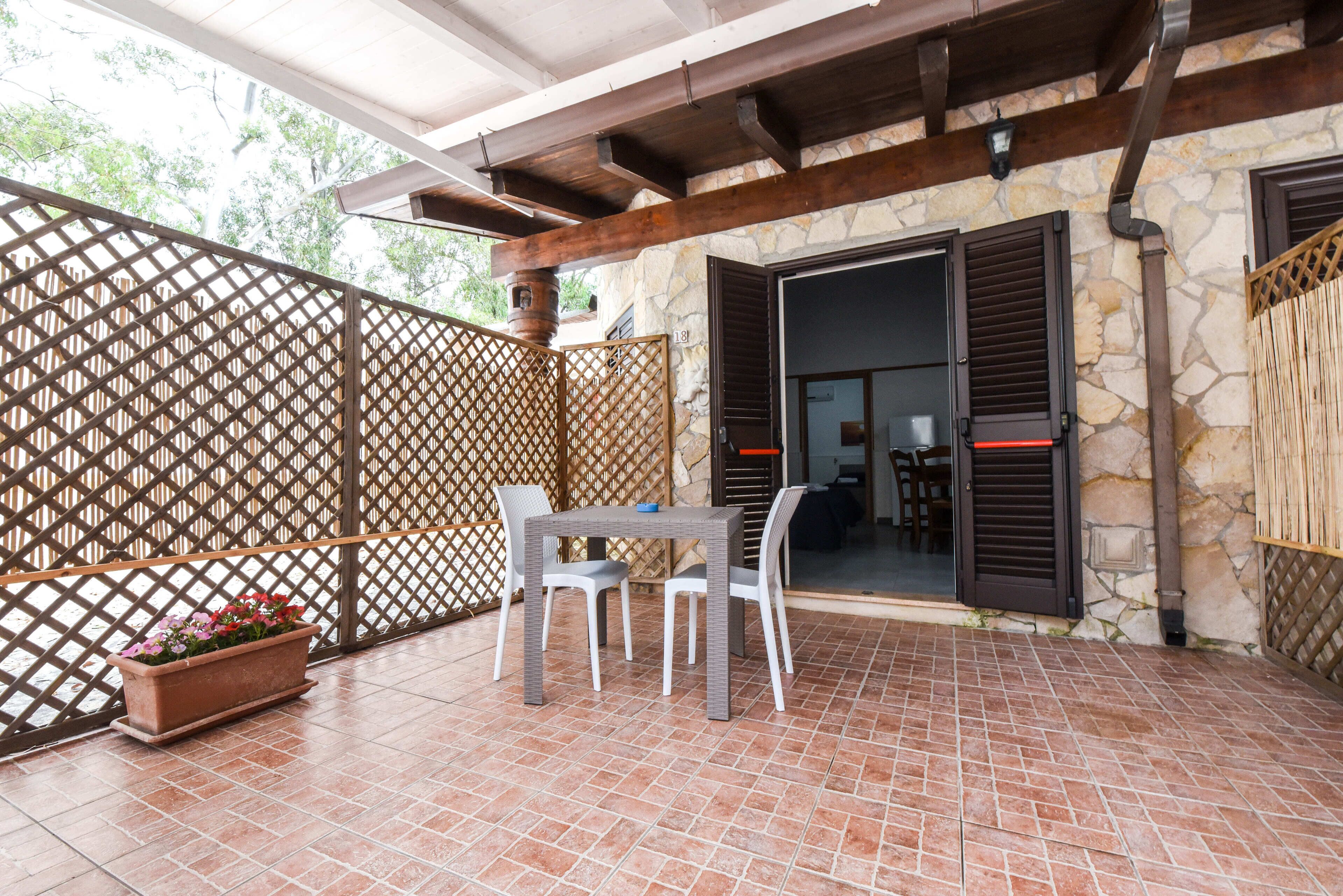 Un patio cubierto con una mesa y sillas, una planta en maceta y un muro de piedra con una puerta.
