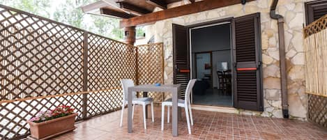 Un patio cubierto con una mesa y sillas, una planta en maceta y un muro de piedra con una puerta.
