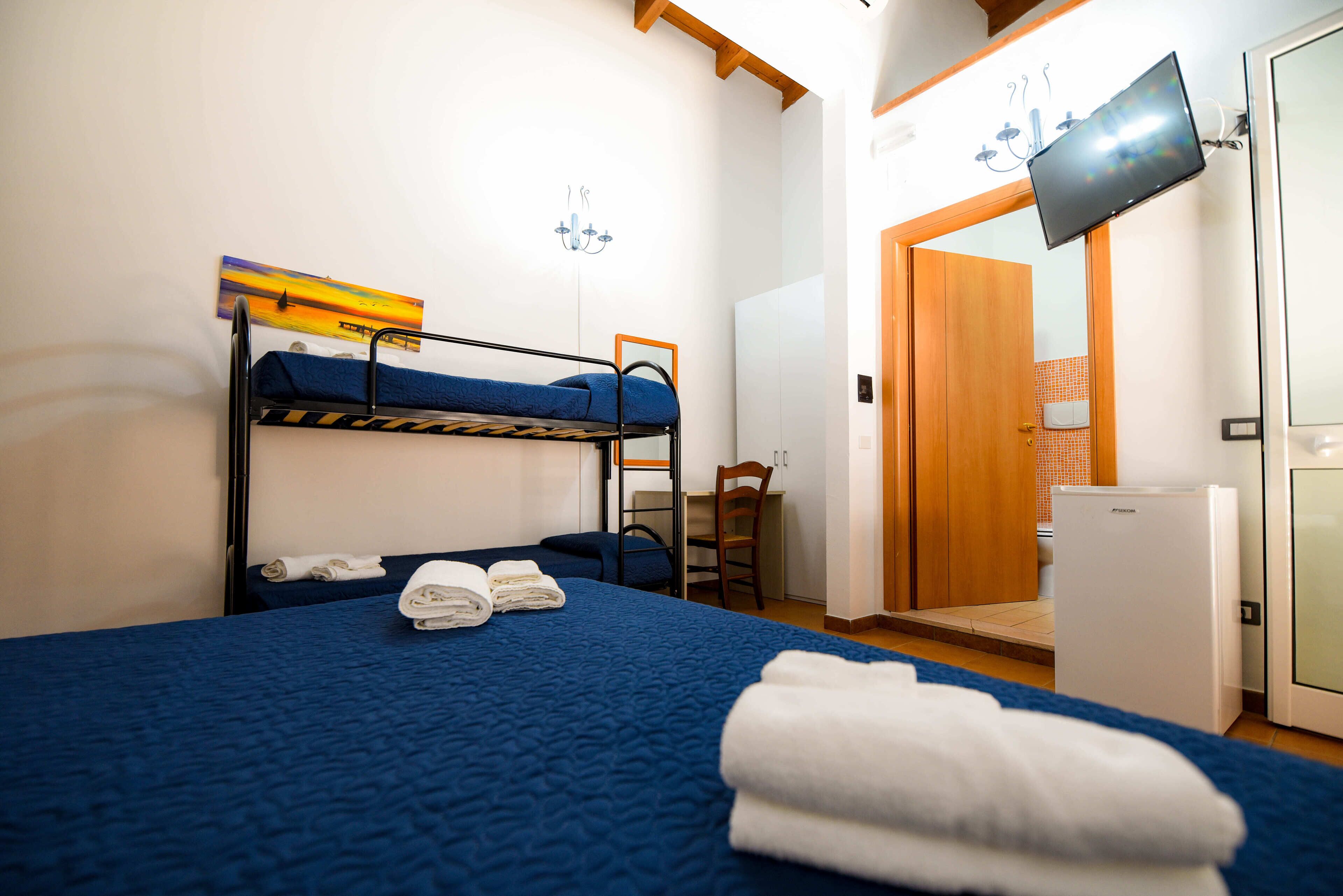 Une chambre avec un lit superposé, un bureau, une chaise, une télévision et un réfrigérateur.
