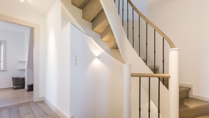 A modern staircase with wooden steps and black balusters, leading to a landing with recessed lighting.