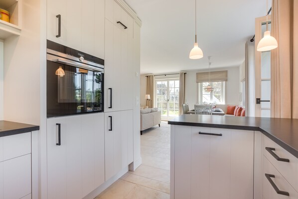 A modern kitchen with white cabinetry, black countertops, and pendant lighting. - Erleben Sie Ihren Urlaub im Typischen Sylt-stil Unter Reet (Wenningstedt-Braderup (Sylt))