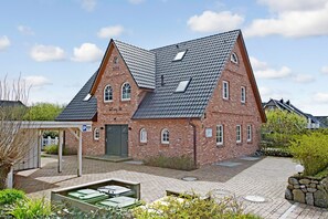 A brick building with a sloped roof, a covered parking area, and a small garden area with a pond. - Modern, Groß, Hell Drei Worte, die Dieses Domizil Perfekt Beschreiben (Wenningstedt-Braderup (Sylt))