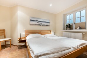 Ein Schlafzimmer mit einem hölzernen Bett, einem Nachttisch, einem Stuhl und einem Fenster mit Jalousien.