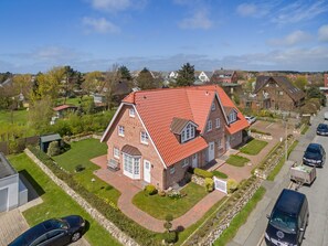 Ein großes Backsteinhhaus mit rotem Ziegeldach, umgeben von einer gepflegten Rasenfläche und einer Auffahrt mit parkenden Autos.