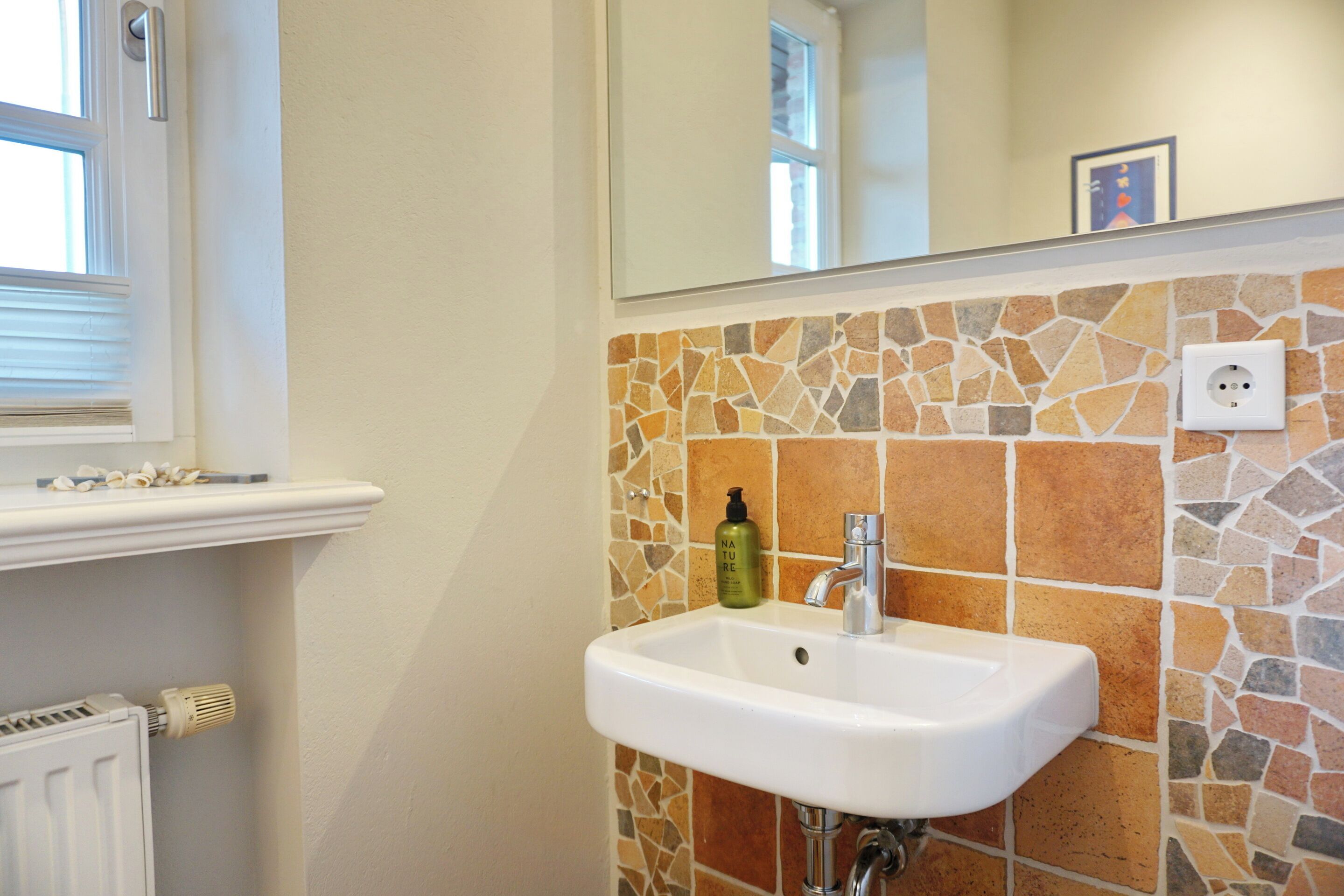 Un baño con lavamanos blanco, salpicadero de azulejos, una ventana y un espejo.