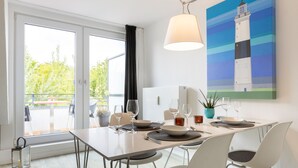 A dining area with a table set for four, a potted plant, and a painting of a lighthouse on the wall.