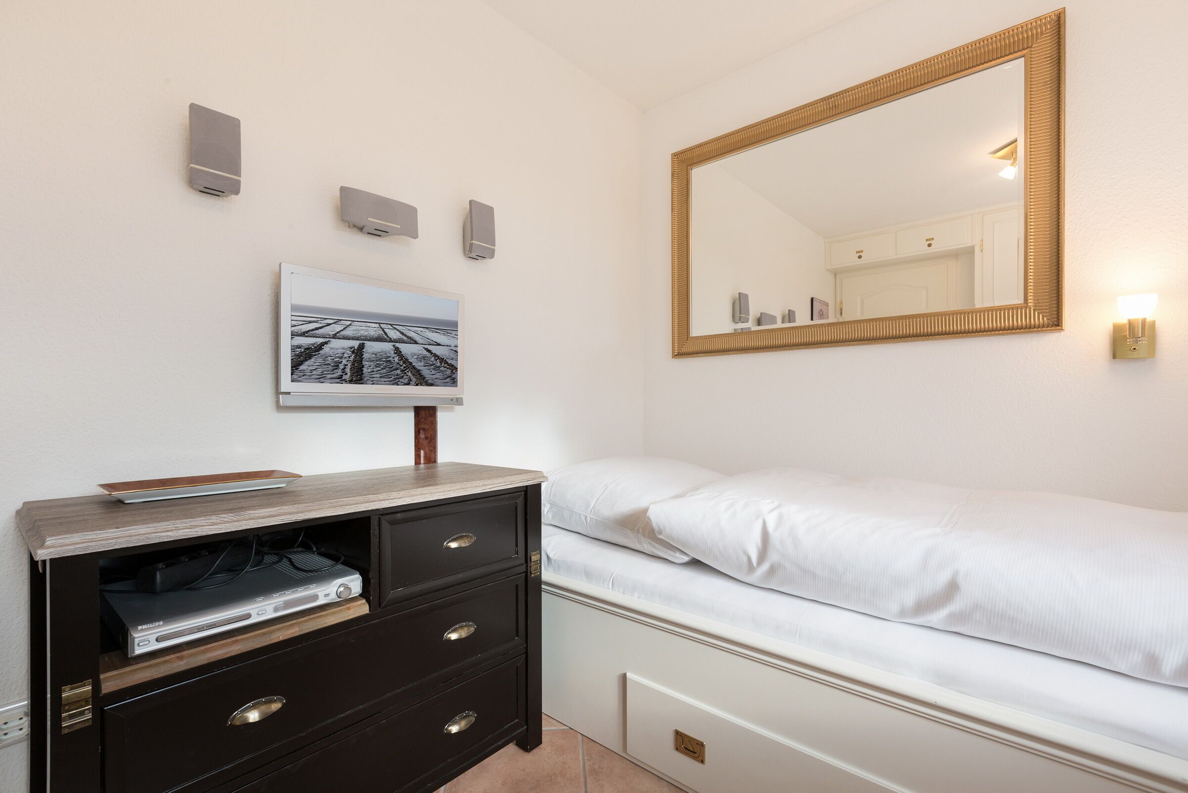 A bedroom with a bed, a dresser with a flat-screen TV, a large mirror, and a framed picture on the wall.