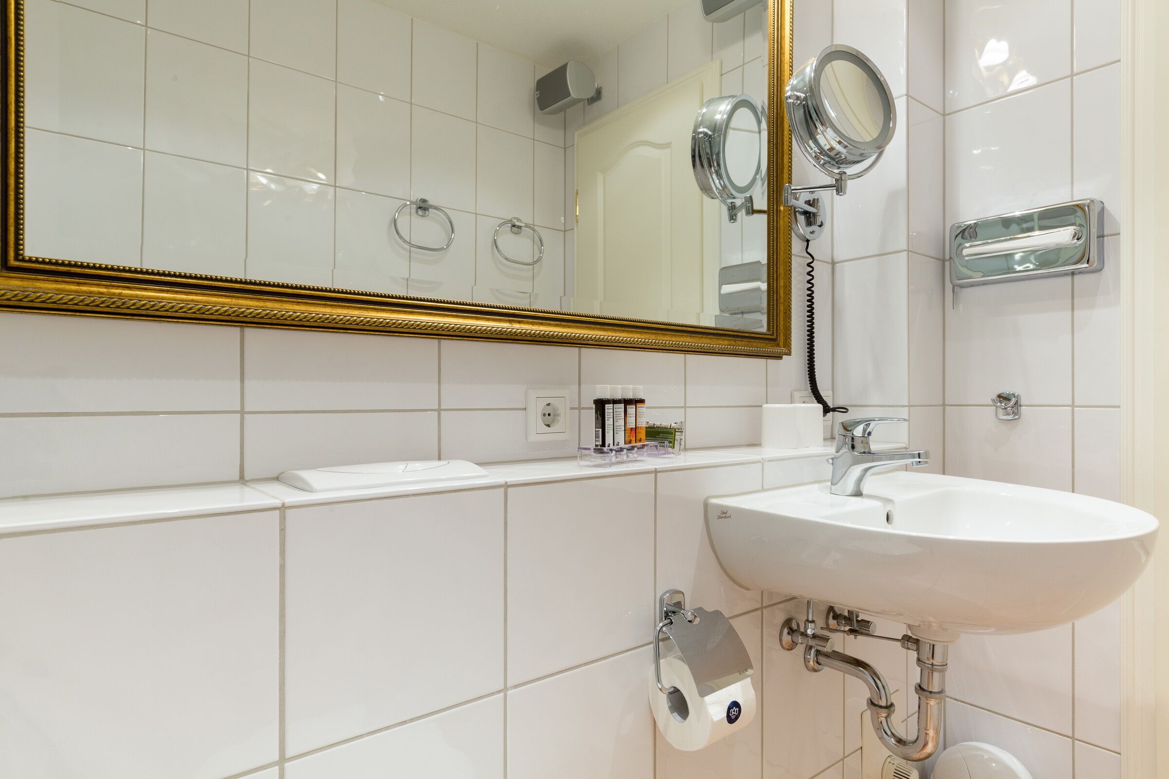 A bathroom with a large mirror, a sink, and a toilet paper holder.
