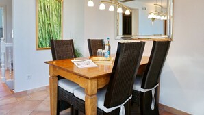 Een eethoek met een houten tafel, rieten stoelen, een grote spiegel en een hanglamp.