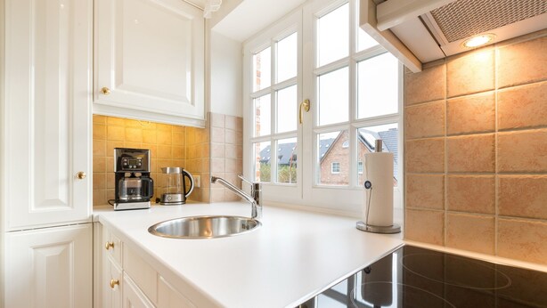 Een moderne keuken met witte kastjes, een roestvrijstalen spoelbak, een koffiezetapparaat en een raam met uitzicht op gebouwen.