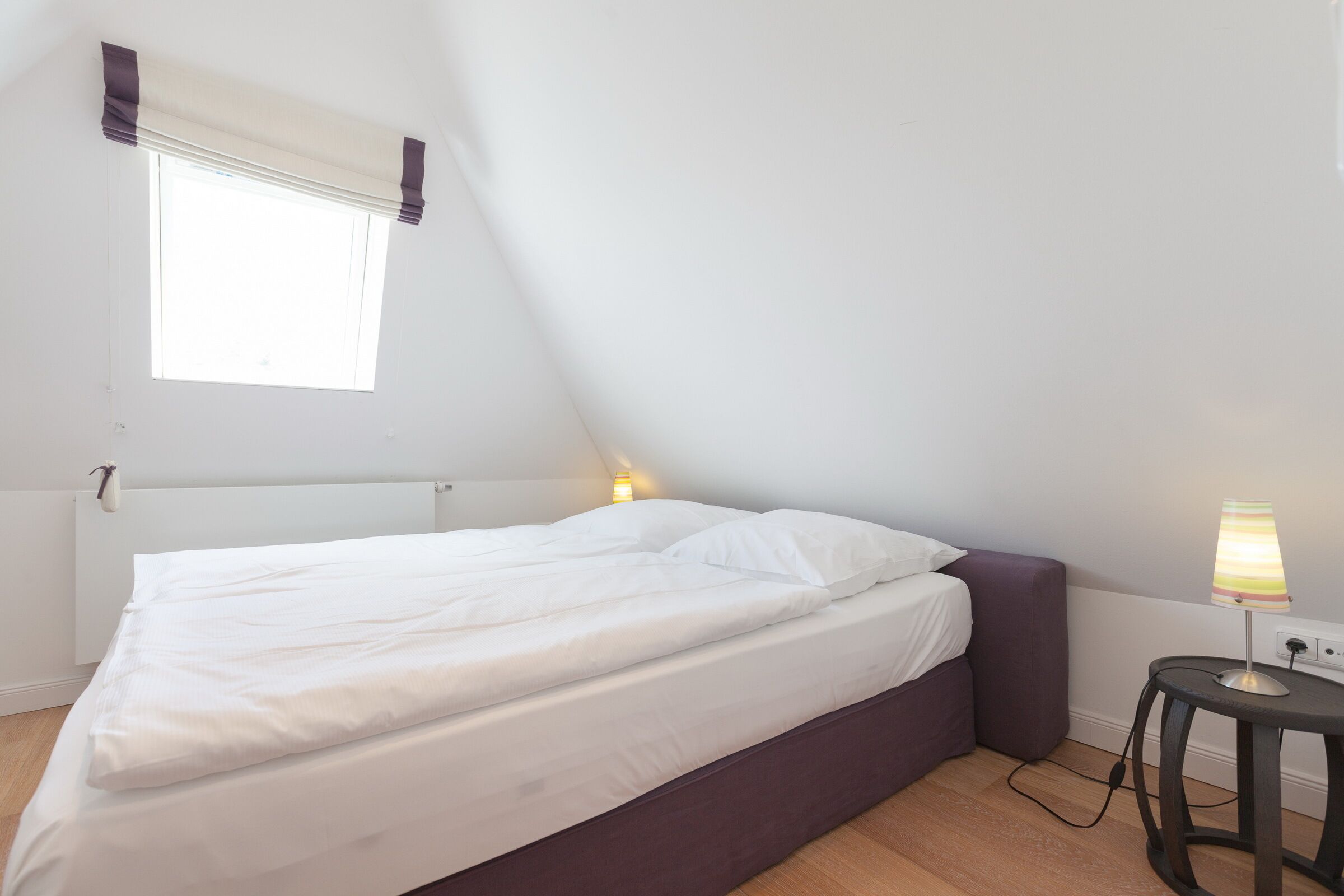 A bedroom with a bed, a bedside lamp, a window with curtains, and a radiator.