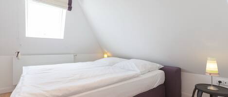 A bedroom with a bed, a bedside lamp, a window with curtains, and a radiator.