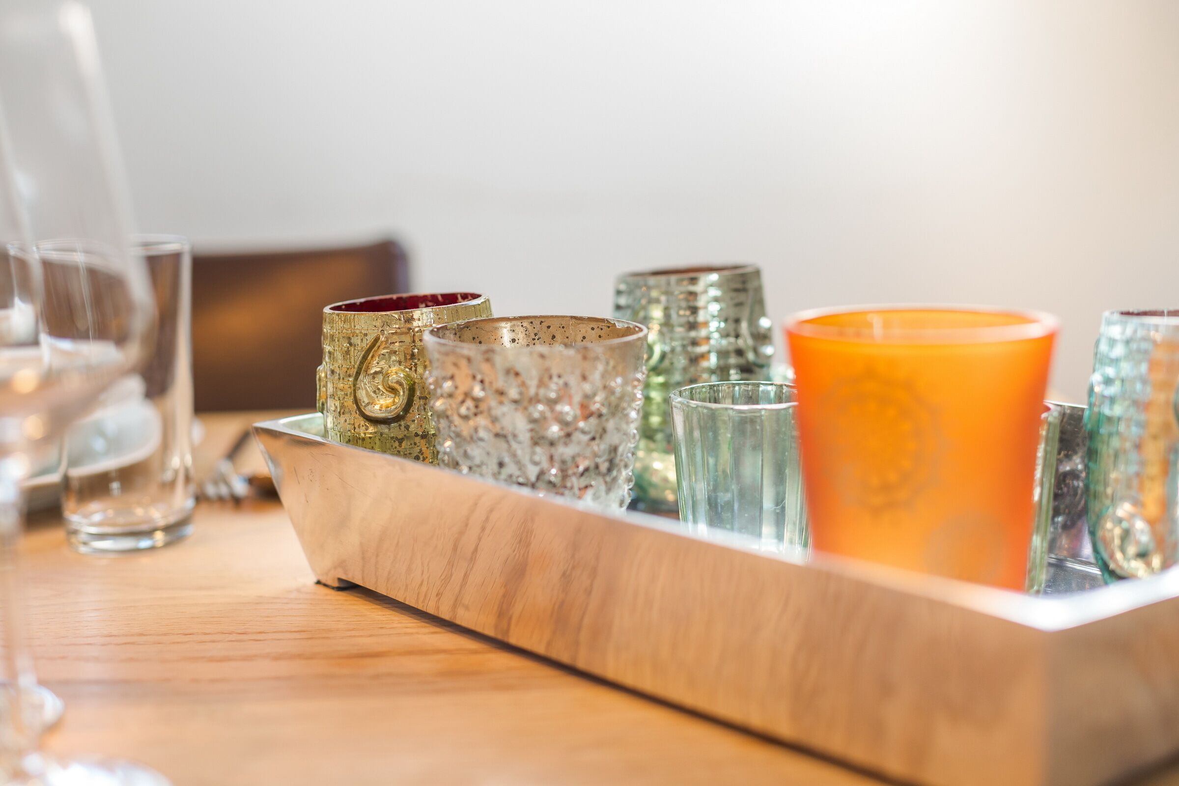 A tray with various glassware, including a large orange candle, on a wooden table.