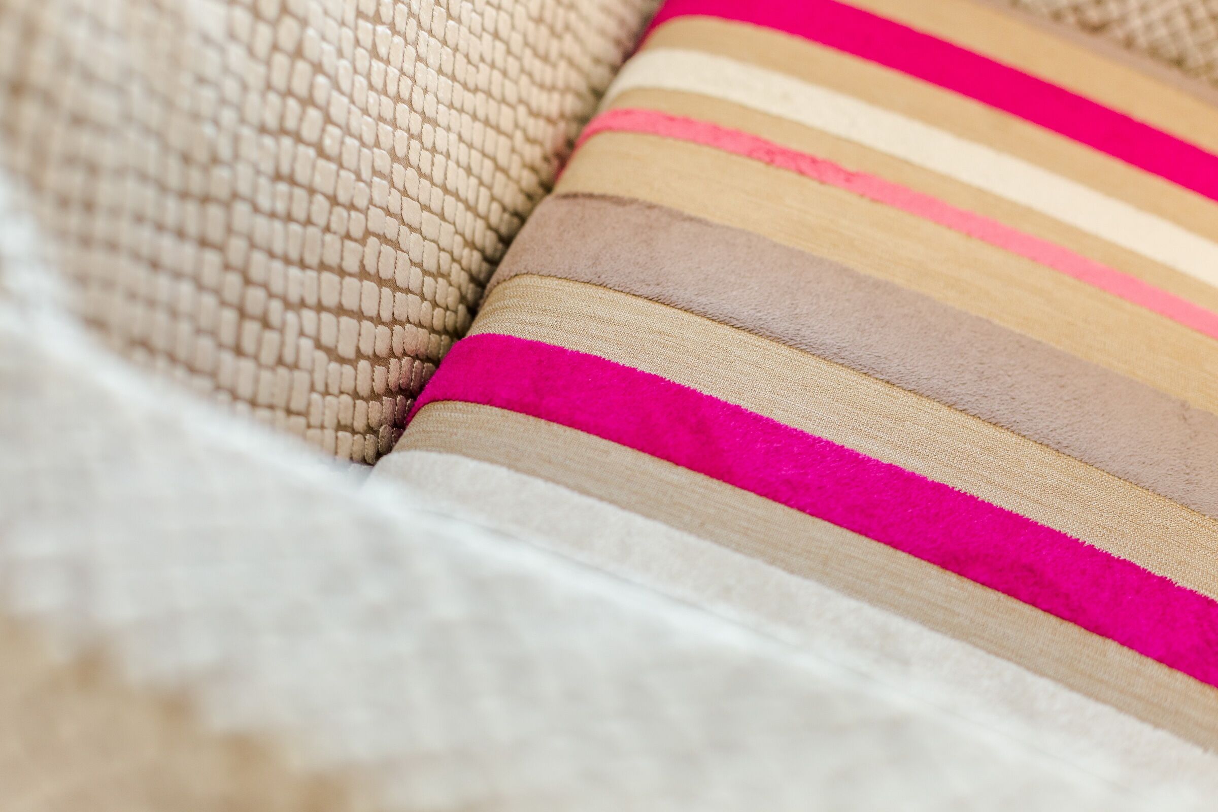 Lähikuva sohvasta, jossa on kuvioitu, beigenvärinen päällinen ja tyyny, jossa on vaakasuoria raitoja beigen, ruskean ja vaaleanpunaisen sävyissä.
