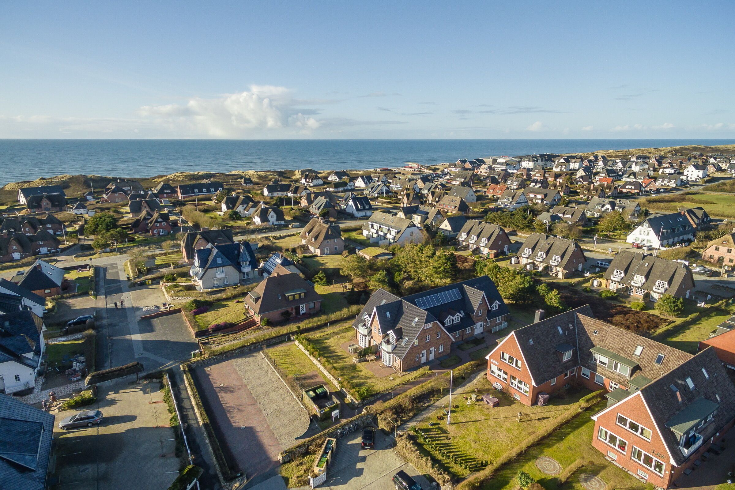 An aerial view of a coastal village with traditional houses, a main road, and a view of the sea.