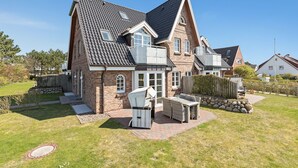Une maison à deux étages, dotée d’un toit en pente, d’une façade en briques et d’un petit patio aménagé avec du mobilier d’extérieur.