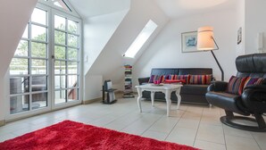 Un salon spacieux avec une grande fenêtre, un canapé en cuir noir, un tapis rouge et une table basse blanche.