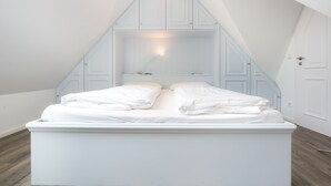 Une chambre avec un lit blanc, un plafond en pente et une armoire intégrée.