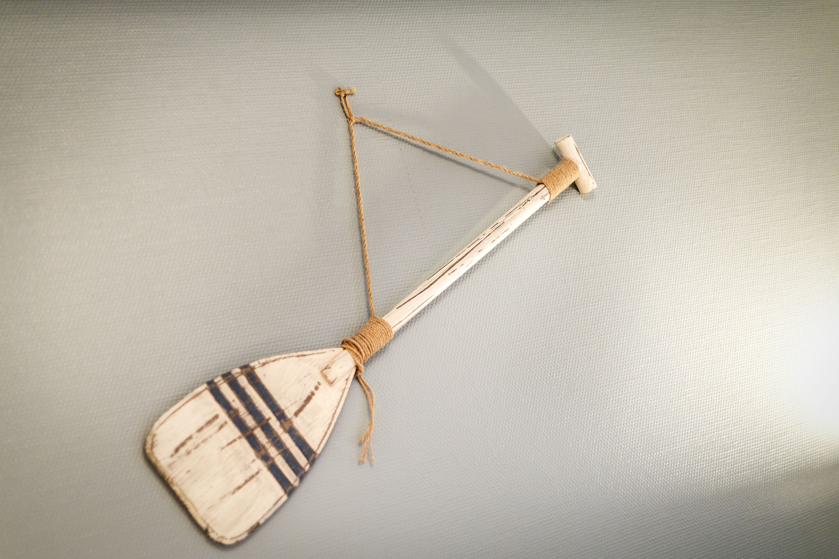 Una pagaia di legno con un manico in corda e un blocco di legno, su una superficie ruvida.