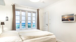A bedroom with a large bed, a TV on the wall, and a window with curtains. - Strandnaher State-of-the-art Luxus (Wenningstedt-Braderup (Sylt))