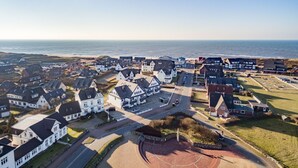 A coastal residential area with houses, a road, and a beach in the background. - Komfortables Appartement im Erd- und Untergeschoss, ca. 50 qm Nutzfläche (Wenningstedt-Braderup (Sylt))