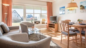 A living room with a sofa, armchair, TV, and dining table with chairs. - Komfortables Appartement im Erd- und Untergeschoss, ca. 50 qm Nutzfläche (Wenningstedt-Braderup (Sylt))