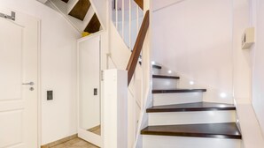 Uma escadaria com degraus de madeira e paredes brancas, conduzindo a uma porta.