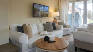 Ein Wohnzimmer mit einer Couch, einem Couchtisch, einem Fernseher und einem Fenster mit Vorhängen.
