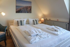 A hotel room with a large bed, two pillows, a chair, a lamp, and a painting on the wall.