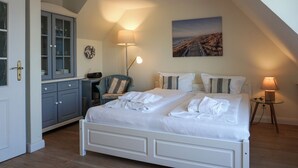 A bedroom with a double bed, a desk with a chair, a lamp, and a painting on the wall. - Urlaub auf der Düne (Wenningstedt-Braderup (Sylt))