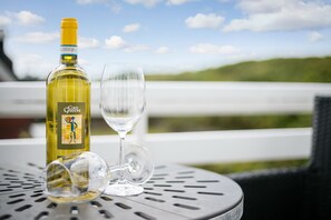 Una botella de vino y una copa vacía sobre una mesa metálica, con vistas a un paisaje verde al fondo.