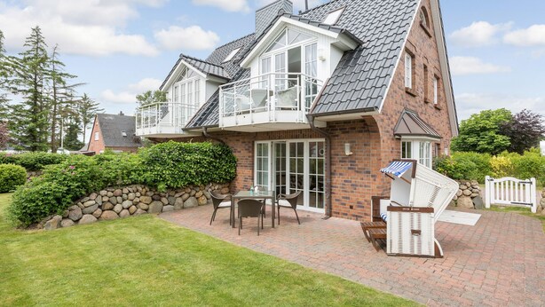 A two-story house with a brick exterior, a balcony, and a patio area with outdoor furniture.