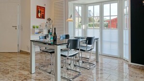 A modern dining area with a glass table, metal chairs, and a view through large windows.